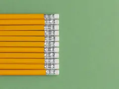 Una fila de lapiceros o portaminas amarillos con gomas de borrar blancas sobre un fondo verde.