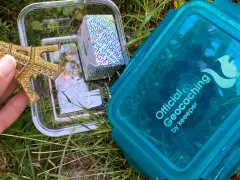 Złoty model Wieży Eiffla w pojemniku, obok niebieskiego pojemnika z napisem "Official Geocaching". To jest geocaching co to za zabawa!