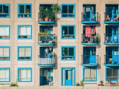 Elegancka loggia i balkon z niebieskimi ramami okiennymi, pełne zieleni i suszącego się prania, tworzą kolorowy kontrast na betonowej fasadzie.