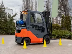 Pomarańczowo-szary wózek widłowy Toyota z butlą gazową, otoczony żółtymi pachołkami, gotowy do testów UDT.