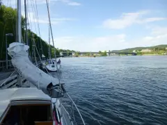 Segelbåtar vid kaj i Lilla Edet, en bro syns i bakgrunden över en bred flod.