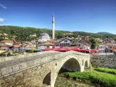 Kamienny most nad rzeką, z widokiem na meczet i miasto na wzgórzu. Kosowo atrakcje turystyczne zachwycają.