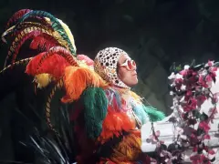 Elton John in einem extravaganten Federkostüm, das an einen Pfau erinnert. Seine ikonischen Elton John Outfits sind legendär.