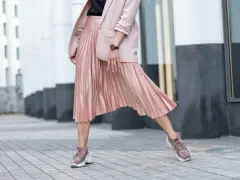 Kobieca stylizacja: różowa plisowana spódnica, marynarka i sportowe buty. Idealne połączenie elegancji i wygody, pokazujące, jakie buty do plisowanej spódnicy pasują najlepiej.