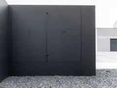 Nowoczesna, czarna skrzynka elektryczna w ogrodzeniu, z dyskretnymi symbolami błyskawicy i kranu.