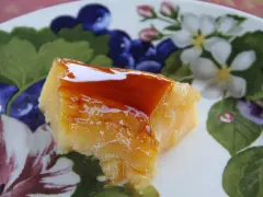 Un trozo de tocino de cielo de la abuela, con su caramelo brillante, sobre un plato decorado con flores y frutos.