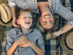 Uśmiechnięta mama i syn leżą na kocu. Idealny dzień na życzenia z okazji Dnia Mamy.