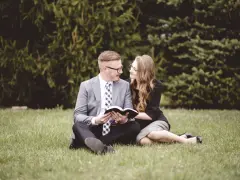 Para młoda siedzi na trawie, czytając razem Biblię. Ich wspólna modlitwa wiernych na ślub jest pełna miłości i nadziei.