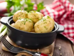 Gotujesz ziemniaki na ból ucha? Te młode ziemniaczki, posypane koperkiem, wyglądają apetycznie. Obok widelec i czerwono-biała serwetka.