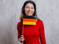 Uśmiechnięta kobieta w słuchawkach trzyma flagę Niemiec. Czy to jej nowy nauczyciel języka niemieckiego?