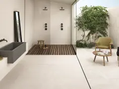 Un bagno moderno con vasca in pietra, doccia a filo pavimento e un'area relax esterna. Il pavimento casa mare crea un'atmosfera rilassante.