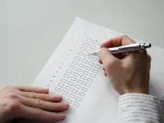 Dłoń z długopisem wypełnia ankietę z polami wyboru.