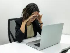 Femme stressée devant son ordinateur, les mains sur les tempes. Une situation difficile, peut-être un licenciement pendant arrêt maladie pour dépression.