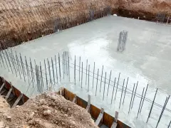 Świeżo wylany beton na fundamencie domu, zbrojenie wystające z płyty. To kluczowy etap, czym wykończyć fundament domu, by był trwały.