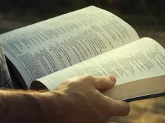 A hand holds open a Bible, revealing the words of Agur in the Bible, Proverbs 31:2.