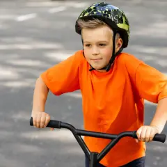 Chłopiec w kasku na rowerze, ubrany na pomarańczowo, z uśmiechem na twarzy. Czy kask na rower jest obowiązkowy? Zawsze warto go mieć!