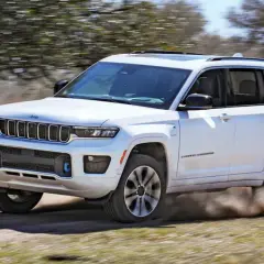 Biały Jeep Grand Cherokee z napędem 4x4 pokonuje piaszczystą drogę, wzbijając tumany kurzu.