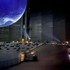 Besucher sitzen auf Tribünen vor einer riesigen Erdkugel in einem Mitmach Museum NRW.