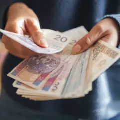 Ręce liczą polskie banknoty. Zastanawiasz się, ile wzrośnie emerytura z OFE po 65 roku życia?