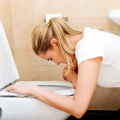 Kobieta pochyla się nad toaletą, czując się źle. Szuka czegoś na wymiotowanie.