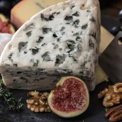 Kawałek ser gorgonzola z niebieską pleśnią, obok figa, orzechy, czosnek i winogrona.