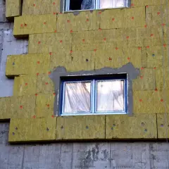 Pannelli isolanti gialli fissati con chiodi rossi mostrano come funziona il cappotto termico su un edificio in costruzione.