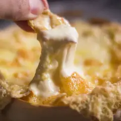 Un morceau de pain trempé dans un fromage fondu doré, prêt à être dégusté. Une invitation à découvrir la recette du Berthoud.