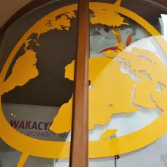 Żółta mapa świata na szybie biura podróży z widocznymi ofertami wakacyjnymi.