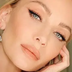 Primo piano di una donna con un elegante trucco occhi, labbra nude e orecchini a cerchio.