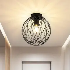 Nowoczesna lampa sufitowa z czarną, drucianą kulą i widoczną żarówką, tworząca ciekawe cienie na suficie.