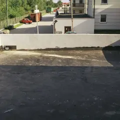 Widok na płaski dach z widocznymi etapami odwodnienia. W tle budynki i drzewa.