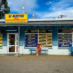Dziewczyna w czerwonej sukience siedzi na ławce przed sklepem "U Krysia", gdzie kręcono "Ranczo".