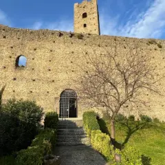 Rovine del castello di Larciano Pistoia, con torre, mura in pietra e un piccolo giardino curato.
