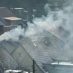 Dym wydobywający się z kominów domów na tle zachmurzonego nieba.