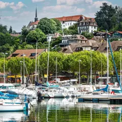 Port de plaisance à Thonon-les-Bains, avec des voiliers blancs et bleus amarrés, des maisons sur la colline et une église. Idéal pour savoir que faire à Thonon-les-Bains.
