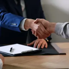 Dwaj mężczyźni ściskają sobie dłonie nad dokumentami, finalizując umowę o dzieło.