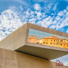 Il MAXXI - Museo Nazionale delle Arti del XXI Secolo riflette edifici storici romani sotto un cielo azzurro e nuvoloso.