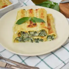 Pyszne cannelloni ze szpinakiem, zapieczone pod beszamelem i serem, ozdobione listkiem bazylii.