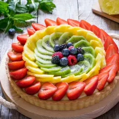 Crostata di frutta con decorazioni colorate di fragole, kiwi, ananas e frutti di bosco.