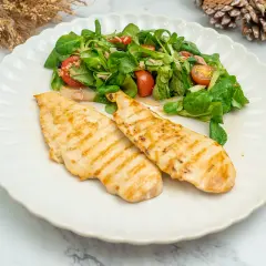 Dos pechugas de pollo a la plancha con marcas de parrilla, servidas con una ensalada fresca de hojas verdes y tomates.