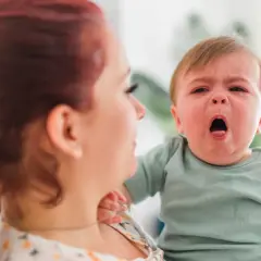 Mama z rudymi włosami tuli płaczące dziecko. Może to być objaw RSV u malucha, który potrzebuje troski.