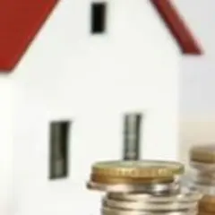 Casa blanca con tejado rojo y pilas de monedas. Representa los gastos de cancelación de hipoteca.