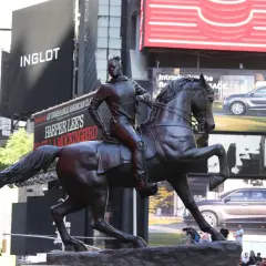 A bronze statue of a person on horseback stands in Times Square, with billboards for Inglot and Harper Lee's "To Kill a Mockingbird" in the background.