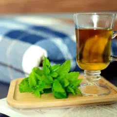 Szklanka herbaty i świeża mięta na drewnianej podstawce. Idealne składniki, by dowiedzieć się, jak parzyć miętę i cieszyć się jej aromatem.