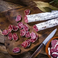 Tranches de saucisson sec, entiers et coupés, sur une planche en bois. On peut cuire du saucisson sec pour le déguster chaud.
