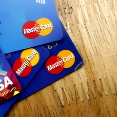 Kilka kart płatniczych, w tym Visa Platinum i karty debetowe z logo MasterCard, leżą na drewnianym blacie.