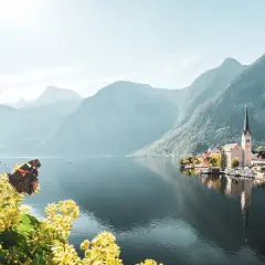 Schmetterling auf blühendem Zweig vor malerischem Dorf am See, umgeben von majestätischem Gebirge Europas.