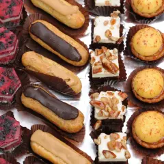 Variedad de petit fours: éclairs de chocolate y caramelo, pastelitos de frutas rojas, cuadrados de crema con nueces, tartas de crema amarilla y pastelitos de chocolate.