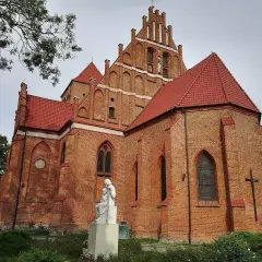 Majestatyczny kościół w Pucku z cegły, z czerwonym dachem i rzeźbą Matki Boskiej.