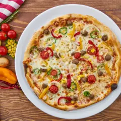 Apetyczna pizza z warzywami i mięsem na talerzu, obok sztućce i składniki.